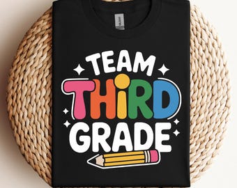 May include: Black t-shirt with the words "TEAM THIRD GRADE" in white, and the word "THIRD" in colorful letters. A yellow pencil with a pink eraser is at the bottom. The shirt is on a woven surface.