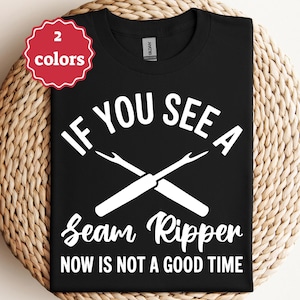 May include: Black t-shirt with white text: "IF YOU SEE A Seam Ripper NOW IS NOT A GOOD TIME." Features a graphic of two crossed seam rippers. A red and white "2 colors" tag is in the upper left corner.