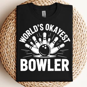 Peut inclure: T-shirt noir avec un motif blanc représentant un jeu de bowling. Le texte "WORLD'S OKAYEST BOWLER" est écrit en blanc. Le t-shirt est en matière souple et convient pour un usage décontracté.