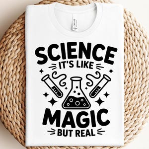 以下が含まれることがあります： 科学をテーマにしたグラフィックが施された白いTシャツ。デザインは、太字の黒い文字で「SCIENCE It's Like MAGIC BUT REAL」という言葉と、ビーカーと試験管のイラストが特徴です。Tシャツは織り込まれた表面に表示されています。
