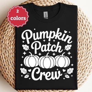May include: Black t-shirt with the words "Pumpkin Patch Crew" in white script, along with three pumpkin illustrations. The shirt also features leaf and star accents. A red tag in the upper left corner indicates "2 colors".