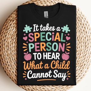 Op de afbeelding: Zwart t-shirt met de kleurrijke tekst "It takes a SPECIAL PERSON to hear What a Child Cannot Say". Het ontwerp bevat puzzelstukjes, hartjes en appels.