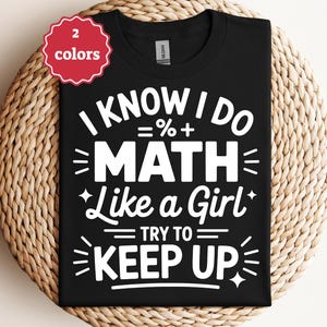Può includere: T-shirt nero con la scritta bianca "I KNOW I DO MATH Like a Girl TRY TO KEEP UP". Un'etichetta rossa circolare in alto a sinistra dice "2 colori". La maglietta è esposta su una superficie tessuta.