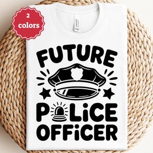 May include: White t-shirt with a black graphic that reads "FUTURE POLICE OFFICER." The design includes a police hat, stars, and a police siren. A red and white sticker in the upper left corner indicates "2 colors."