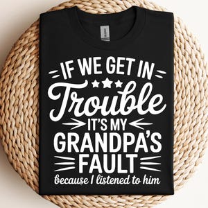 May include: Black t-shirt with white text that reads "IF WE GET IN Trouble IT'S MY GRANDPA'S FAULT because I listened to him." The shirt is folded on a woven surface.