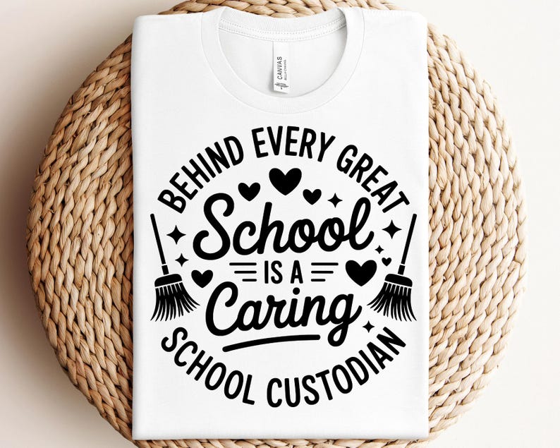 May include: White t-shirt with a crew neck featuring a black graphic. The graphic reads "BEHIND EVERY GREAT SCHOOL IS A CARING SCHOOL CUSTODIAN" with hearts, stars, and brooms. The shirt is displayed on a woven surface.
