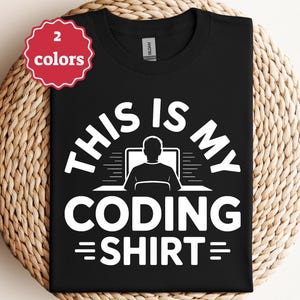 Könnte beinhalten: Schwarzes T-Shirt mit dem weißen Text "THIS IS MY CODING SHIRT", das eine Silhouette einer Person zeigt, die an einem Computer arbeitet. Ein rot-weißes Etikett weist auf die Verfügbarkeit von zwei Farben hin.