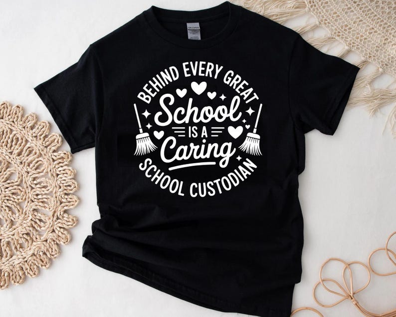 May include: Black t-shirt with a white graphic that reads "BEHIND EVERY GREAT SCHOOL IS A CARING SCHOOL CUSTODIAN." The design includes hearts and brooms. The shirt is made of a soft material.