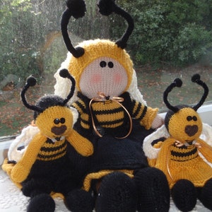 Peut inclure: Trois poupées abeilles en tricot, une grande et deux plus petites. La grande poupée porte une robe noire à rayures jaunes et noires. Les plus petites poupées portent des robes à rayures jaunes et noires. Les trois poupées ont des yeux noirs et des nez bruns.