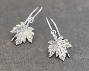 May include: A pair of silver dangle earrings featuring a detailed maple leaf design.