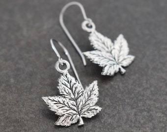 May include: A pair of silver dangle earrings featuring a detailed maple leaf design. The leaves are textured and have a slightly oxidized finish.