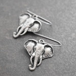 May include: A pair of silver elephant earrings with a detailed design. The earrings are dangle style with a simple wire hook.