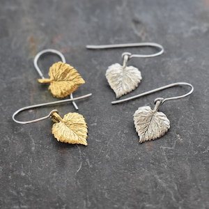 May include: A pair of earrings featuring a leaf design. One earring is gold and the other is silver.