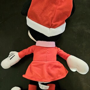 Puede incluir: Un juguete de peluche rojo de Minnie Mouse vestida con un traje de Pap&aacute; Noel rojo con ribetes blancos. Lleva un gorro rojo con ribetes blancos y guantes blancos.