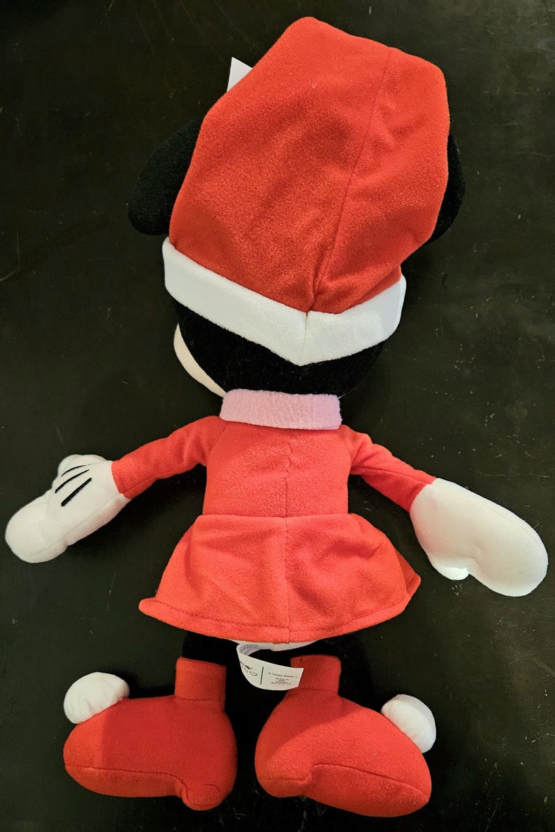 Puede incluir: Un juguete de peluche rojo de Minnie Mouse vestida con un traje de Pap&aacute; Noel rojo con ribetes blancos. Lleva un gorro rojo con ribetes blancos y guantes blancos.