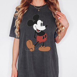 May include: Dark grey t-shirt featuring a classic Mickey Mouse graphic. The cartoon character is depicted in black, white, red, and brown. The word "Pepper" is written in cursive in the upper right corner.
