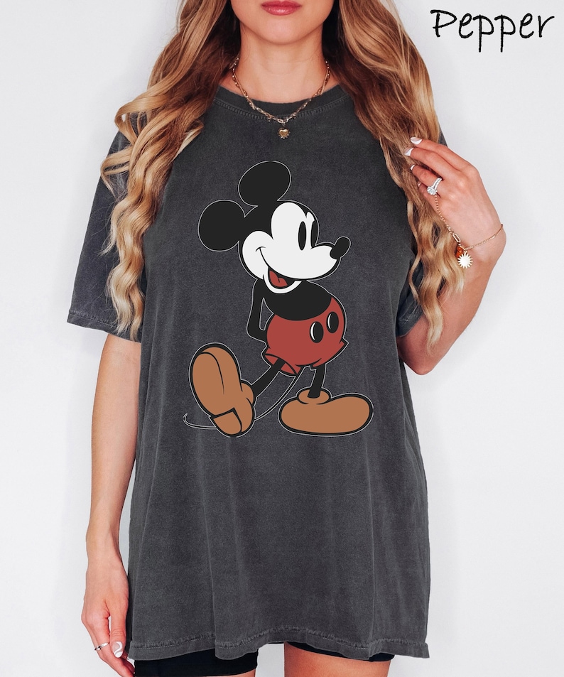 May include: Dark grey t-shirt featuring a classic Mickey Mouse graphic. The cartoon character is depicted in black, white, red, and brown. The word "Pepper" is written in cursive in the upper right corner.