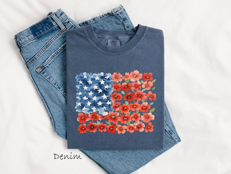May include: A navy blue t-shirt with a watercolour design of the American flag. The flag design features white stars on a blue background and red flowers. The word "Denim" is printed at the bottom.