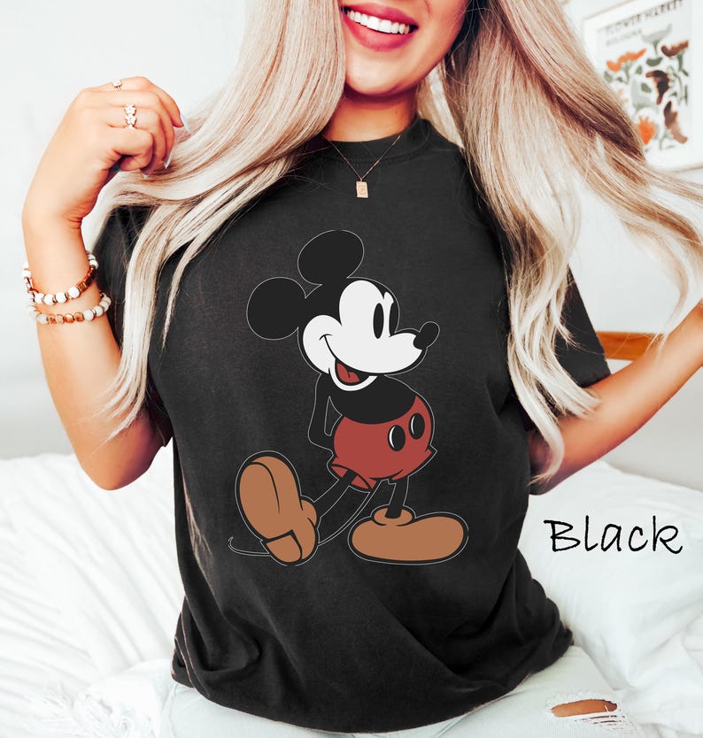 May include: Black t-shirt featuring a classic Mickey Mouse graphic. The cartoon character is depicted in his signature colors: black, red, white, and brown. The word "Black" is printed in white on the lower right side of the shirt.