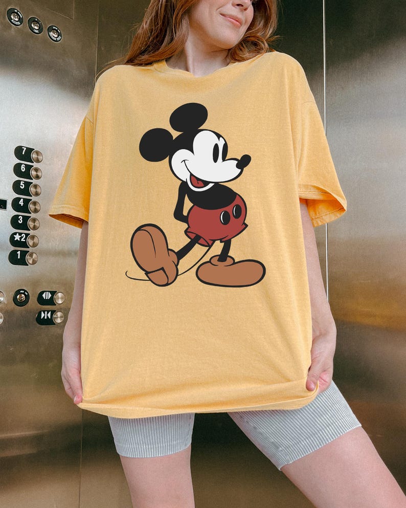 May include: Yellow t-shirt featuring a classic Mickey Mouse graphic. The cartoon character is depicted in black, white, red, and brown. The shirt has short sleeves and a relaxed fit, perfect for casual wear.