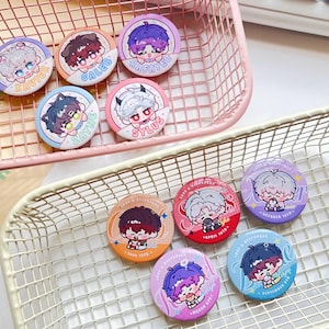 May include: Nine round pins with colorful backgrounds and cartoon illustrations of characters with different hairstyles and clothing. Each pin has text on it, including names like "Javier", "Caleb", "Sylus", and "April Tenth".