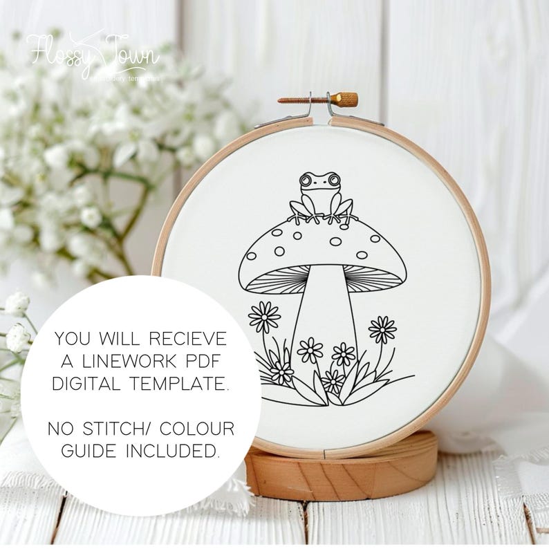 May include: A black and white line drawing of a frog sitting on a mushroom with a white background. The image is in a round embroidery hoop.