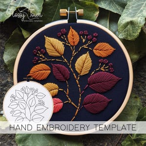 May include: A hand embroidery template featuring a colorful autumn leaf design. The leaves are stitched in shades of gold, orange, and burgundy on a navy blue background. The text "HAND EMBROIDERY TEMPLATE" is displayed below the embroidery hoop.