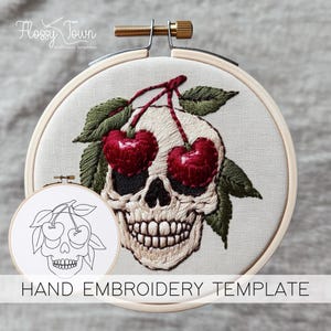 May include: Hand embroidery template featuring a skull with cherries for eyes. The template is printed on white fabric and includes a black and white line drawing of the design.
