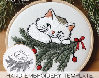 May include: A hand embroidery template featuring a white cat peeking out from behind a green Christmas tree branch with red ornaments. The template is in a white embroidery hoop with a wooden frame. The text "HAND EMBROIDERY TEMPLATE" is at the bottom of the image.