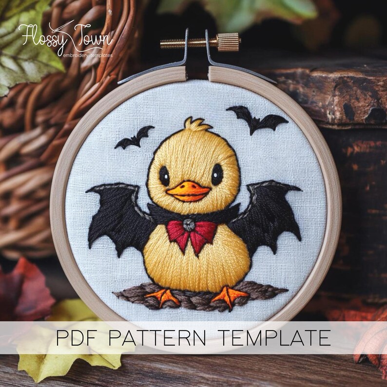 May include: Embroidery pattern template featuring a cute yellow duck with black bat wings and a red bow tie. The duck is sitting on a brown branch with two bats flying above. The pattern is on a white fabric background.