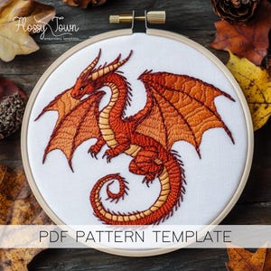 May include: Embroidered pattern template of a red dragon with orange wings, in a wooden embroidery hoop. The template is for a PDF pattern.