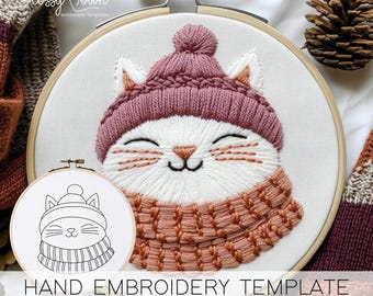 May include: Hand embroidery template featuring a white cat wearing a pink knitted hat and a peach-colored scarf. The template is in a white embroidery hoop with the text "HAND EMBROIDERY TEMPLATE" below.