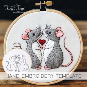 May include: Hand embroidery template featuring two gray mice with pink ears and noses, holding a red heart. The template is in a wooden embroidery hoop with white fabric. The text "HAND EMBROIDERY TEMPLATE" is below the hoop.