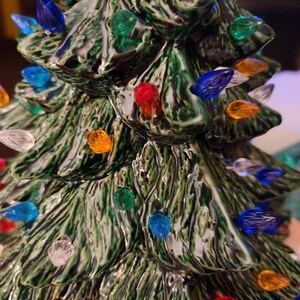 May include: A ceramic Christmas tree with a green glaze and multi-colored lights. The lights are in various colors, including red, blue, green, yellow, and white.