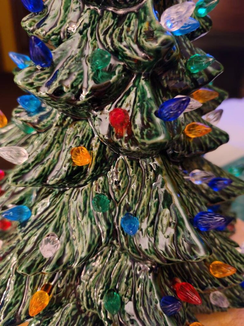 May include: A ceramic Christmas tree with a green glaze and multi-colored lights. The lights are in various colors, including red, blue, green, yellow, and white.