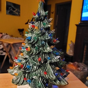 May include: A ceramic Christmas tree with a green glaze and a white base. The tree is decorated with colorful lights and a red star on top.