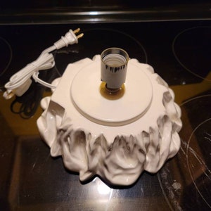 May include: White ceramic Christmas tree base with a ruffled edge and a light socket in the center. A white electrical cord with a plug is attached to the base.