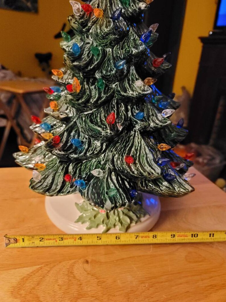 May include: A ceramic Christmas tree with a green glaze and multi-colored lights. The tree is 11 inches tall and has a white base.