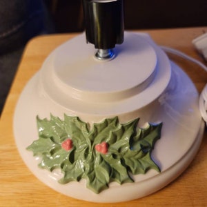 May include: White ceramic Christmas tree stand with a holly leaf design and a black light socket.