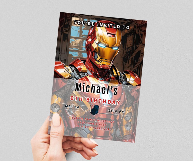 May include: A birthday invitation featuring Iron Man. The invitation has a red and gold color scheme with the text "YOU'RE INVITED TO Michael's 6TH BIRTHDAY MAY 16 6:00 PM". The invitation is held by a person.