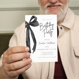 May include: A white invitation card with a black watercolor bow and the words "Birthday Party" in elegant script. The card also includes event details: date, time, and location. The invitation is held by a person.
