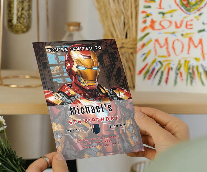 May include: An invitation card featuring Iron Man's helmet and suit design. The card reads "You're invited to Michael's 6th Birthday" with the date and time. The background includes a shelf and a colorful drawing.