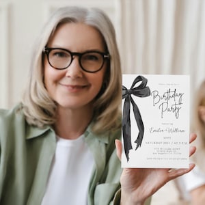 May include: A white invitation card with a black bow and the words "Birthday Party" in elegant script. The card also includes event details such as the date, time, and names "Emilia & William".