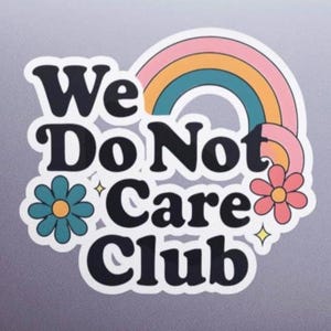 May include: A sticker on a laptop with the text "We Do Not Care Club" in a retro font. The design includes a rainbow, flowers, and stars in pastel colors. The sticker is white with a black outline.