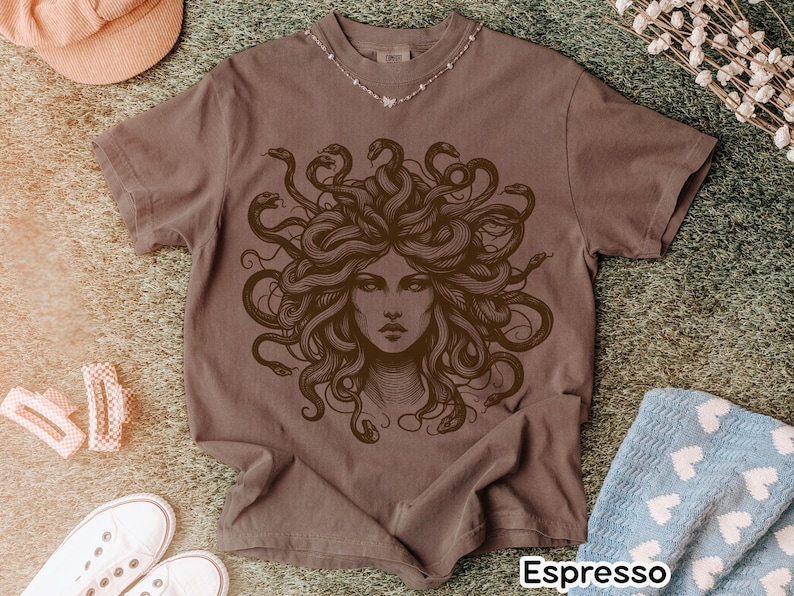 May include: Espresso-colored t-shirt featuring a detailed illustration of Medusa with snakes for hair. The graphic is in a darker brown shade. The shirt has short sleeves and a crew neck. The word "Espresso" is printed at the bottom of the shirt.