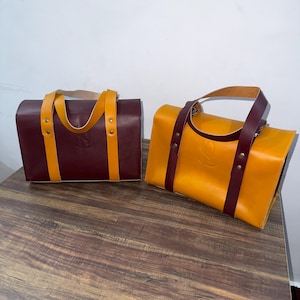 Peut inclure: Deux sacs fourre-tout en cuir, l'un bordeaux avec des sangles jaunes et l'autre jaune avec des sangles bordeaux.