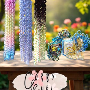 May include: Three colorful curly hair extensions in shades of pink, blue, and black with ombre effects. Decorative wire art pieces are also on display. The image is set on a wooden table with the text "Corby Curl".