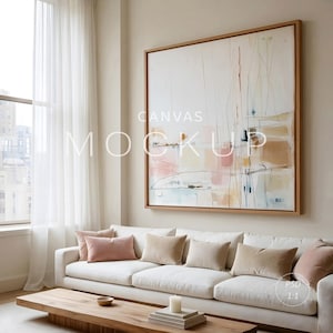 May include: A large square canvas art piece with a wooden frame hangs above a white sofa with several pillows. The artwork features abstract shapes in pink, beige, and blue hues. The words "CANVAS MOCKUP" are printed on the canvas.