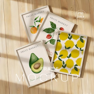 May include: Four framed art prints with fruit illustrations. The prints feature oranges, strawberries, lemons, and an avocado. Each print has the words "FRUIT MARKET" at the top. The frames are white, and the background is a light wood.