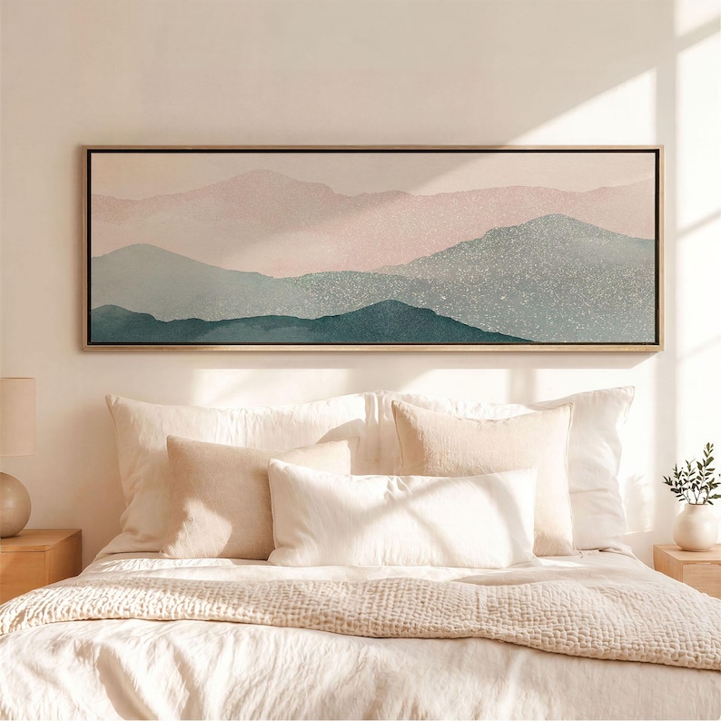 May include: A rectangular landscape wall art piece featuring layered mountain silhouettes in shades of soft pink, muted sage green, and deep teal. The artwork is enclosed in a thin, light-toned wooden frame and hangs horizontally above a bed.